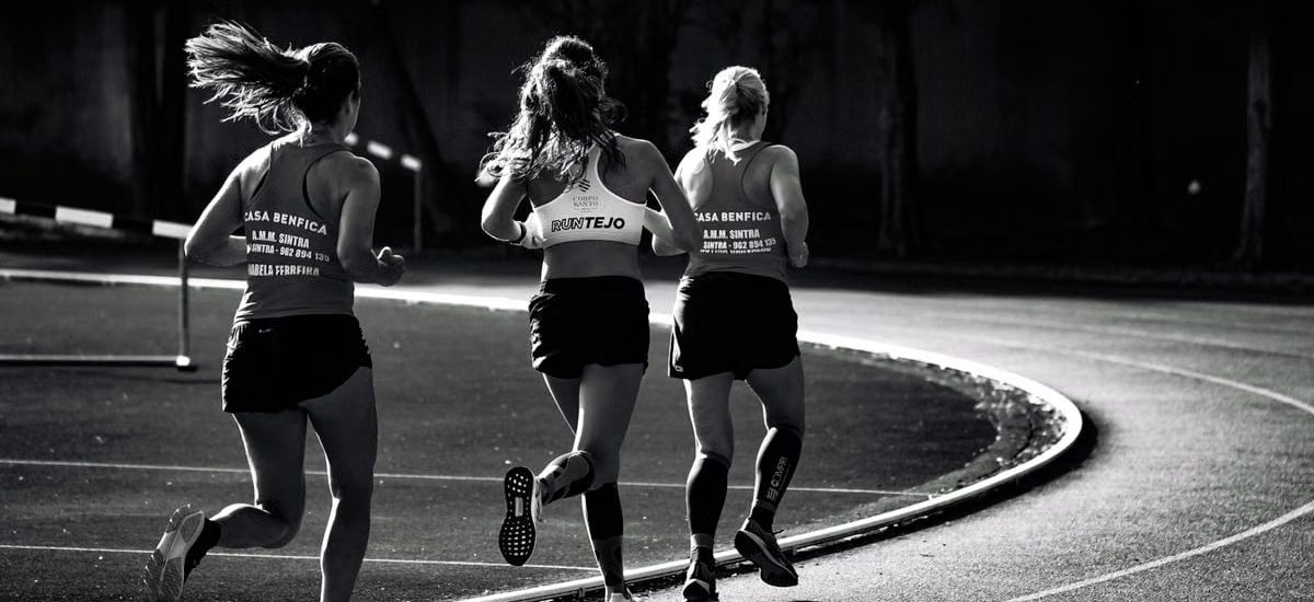 Black and white back view of unrecognizable fit female runners in sportswear running during track and field competition