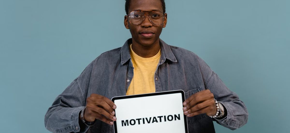 A young African American man holding a tablet displaying the word 'MOTIVATION' against a blue background.